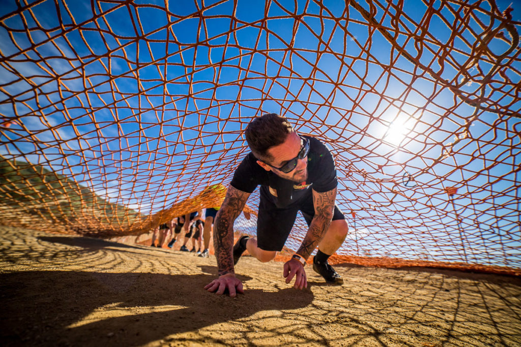Participant crawling under the net while smiling in the heat of the sun