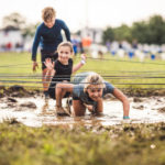 Kid participants crawling in the mud while avoiding the net